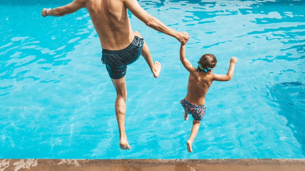 Father and son holding hands and jumping into a pool